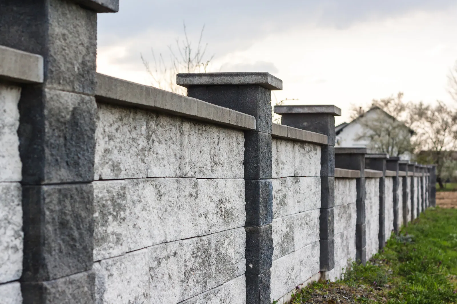 Gray concrete block perimeter wall with pillar caps in a residential area, illustrative photo