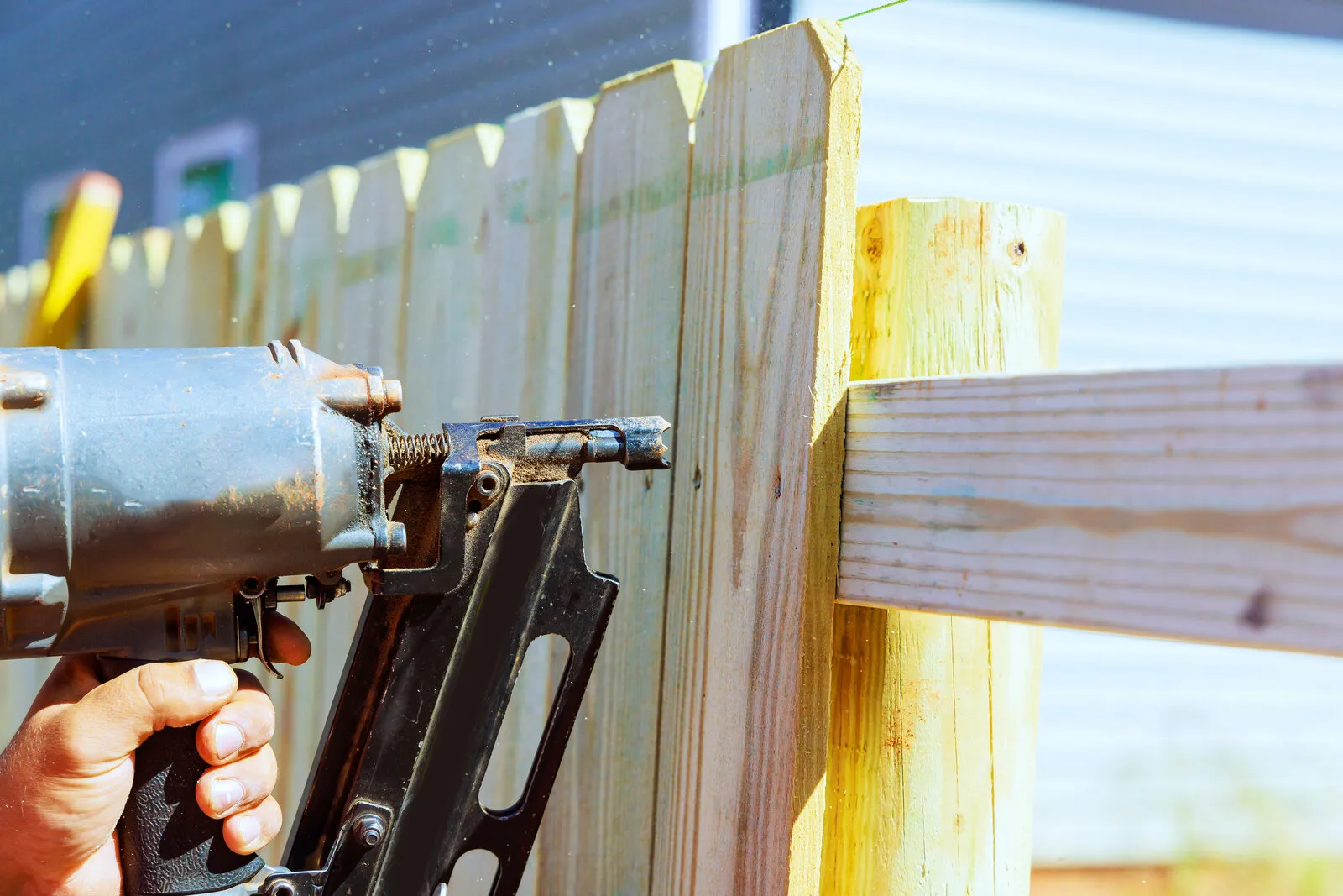 Contractor using a nail gun to attach wood fence boards during a repair, illustrative photo